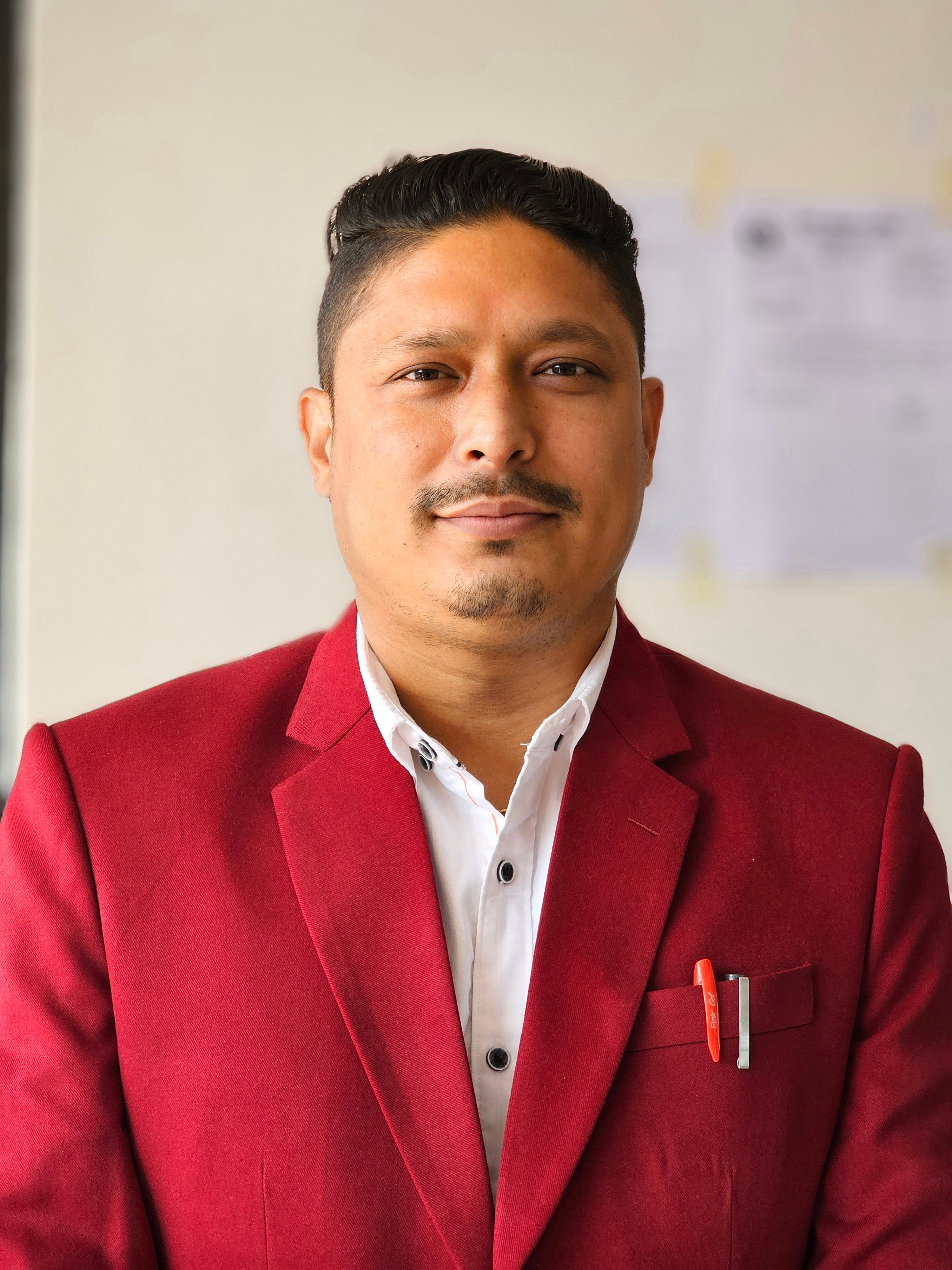 Portrait of a confident young man in a red jacket and white shirt indoors.