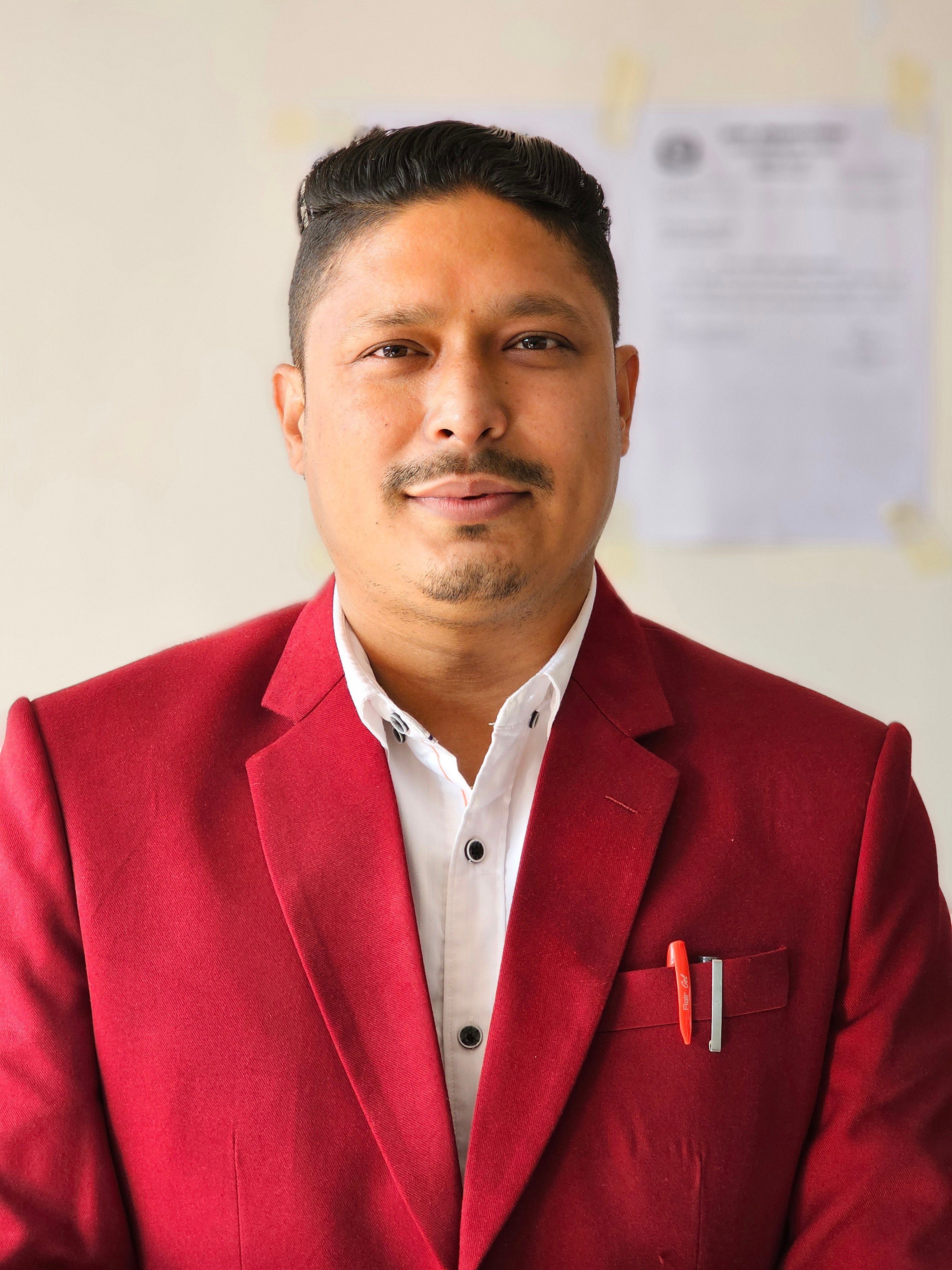 Portrait of a confident man wearing a red jacket and white shirt with a neutral background.