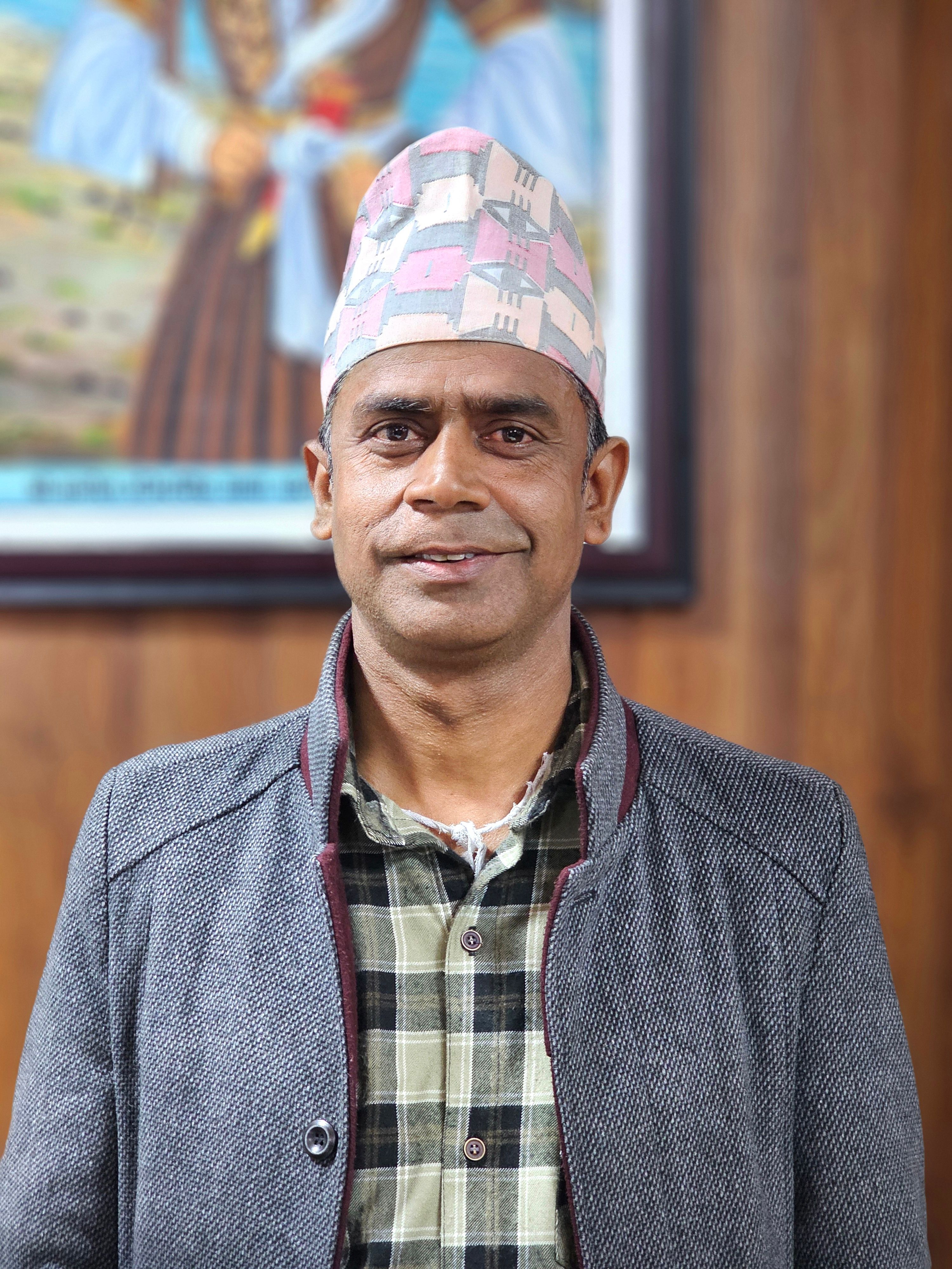 Man wearing a traditional hat and checkered shirt poses indoors for a portrait.