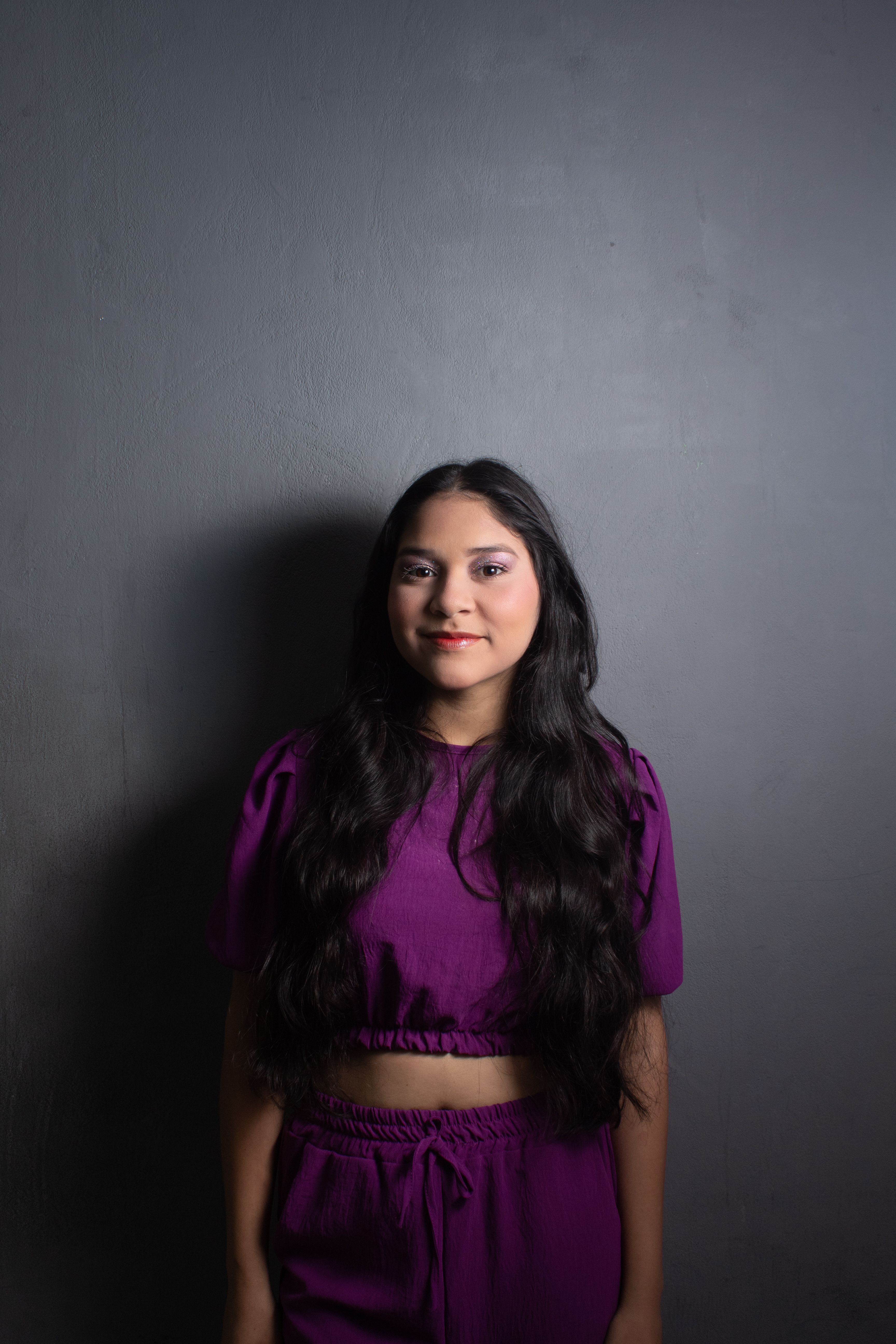 Stylish portrait of a young woman wearing a purple outfit against a black background.
