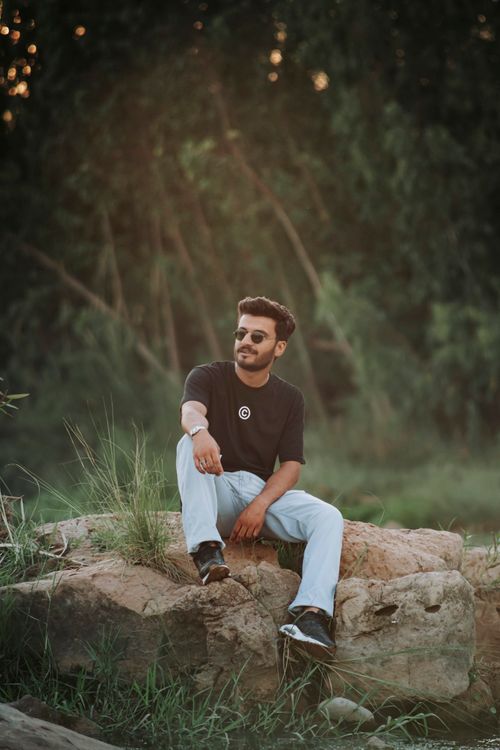 Free Stylish young man posing on rocks in outdoor setting wearing casual attire. Stock Photo
