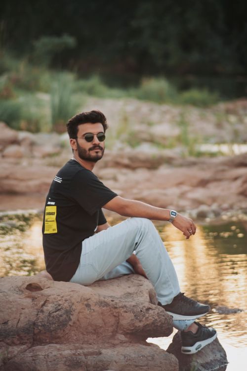 Free A casually dressed man sits by a riverside, enjoying a peaceful summer day. Stock Photo
