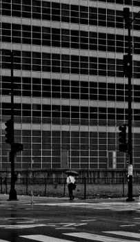 Black and white photo of a person with an umbrella walking in rainy Chicago streets.