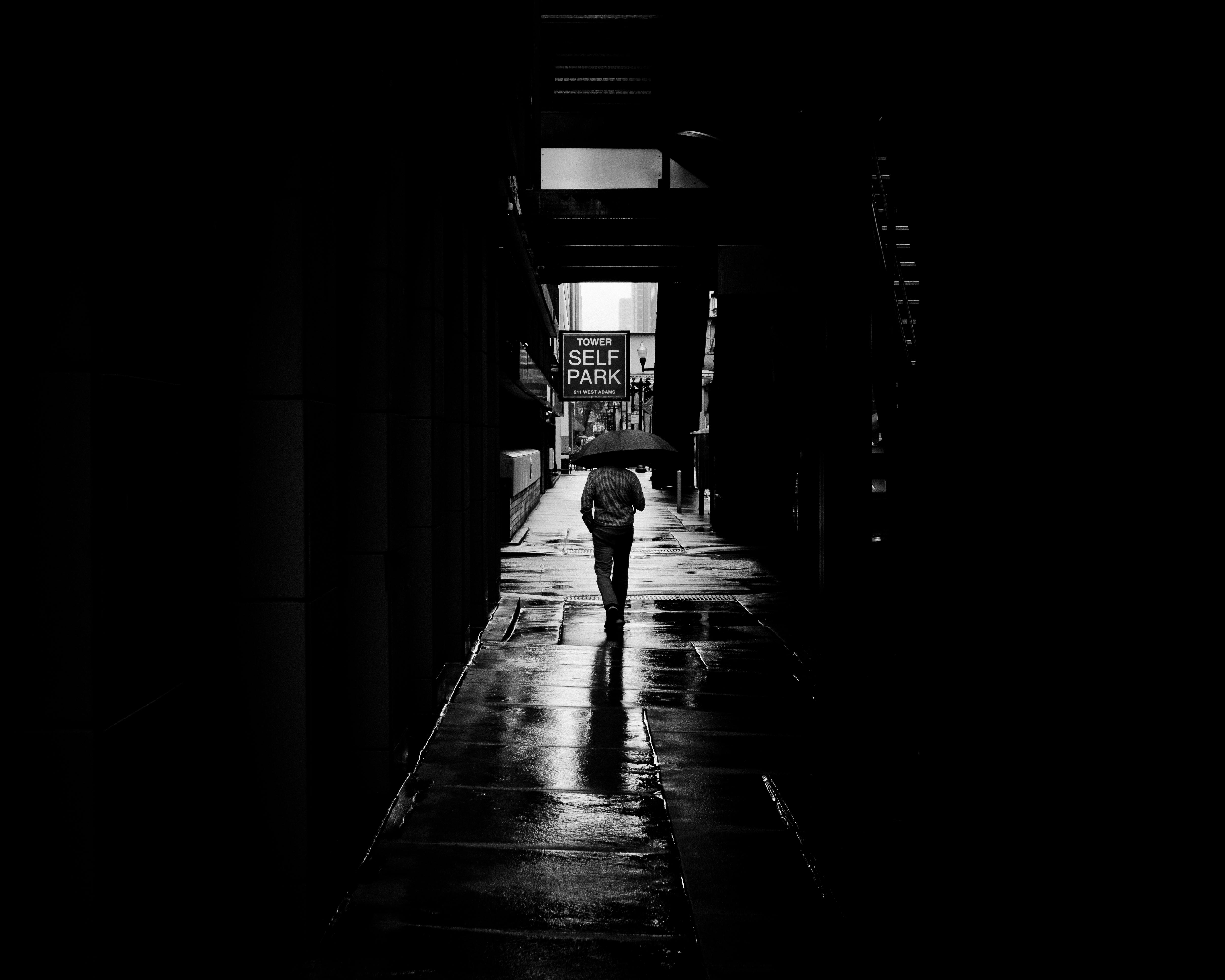 Black and white photo of a solitary pedestrian with umbrella in a Chicago alley.