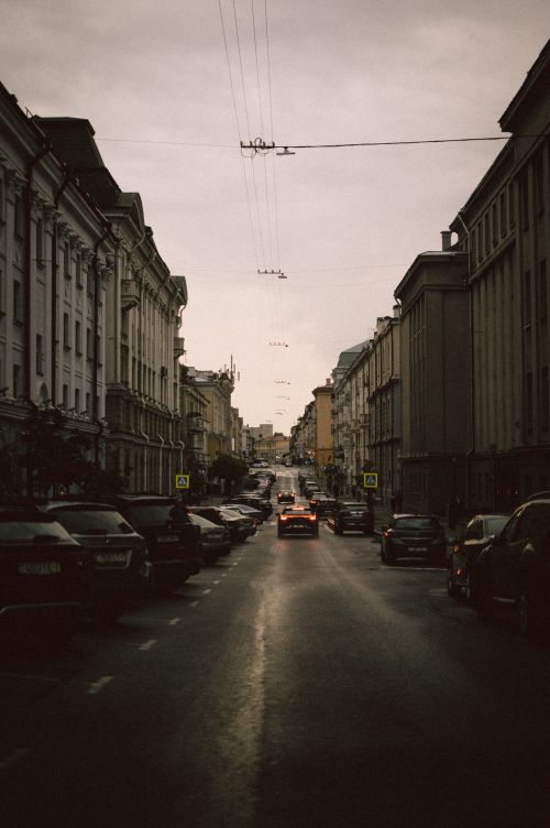 Free Serene city street with cars parked along the classic architecture under a cloudy sky. Stock Photo