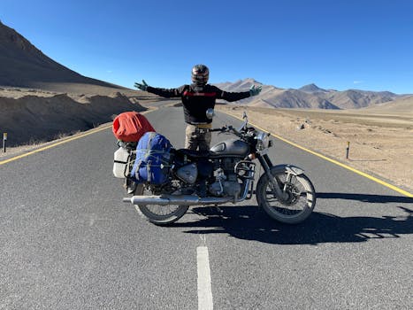 An adventurous motorcyclist stands on an empty road in Leh, arms spread wide, embodying freedom and journey.