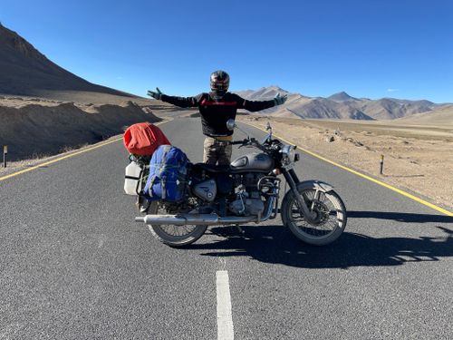 Free An adventurous motorcyclist stands on an empty road in Leh, arms spread wide, embodying freedom and journey. Stock Photo