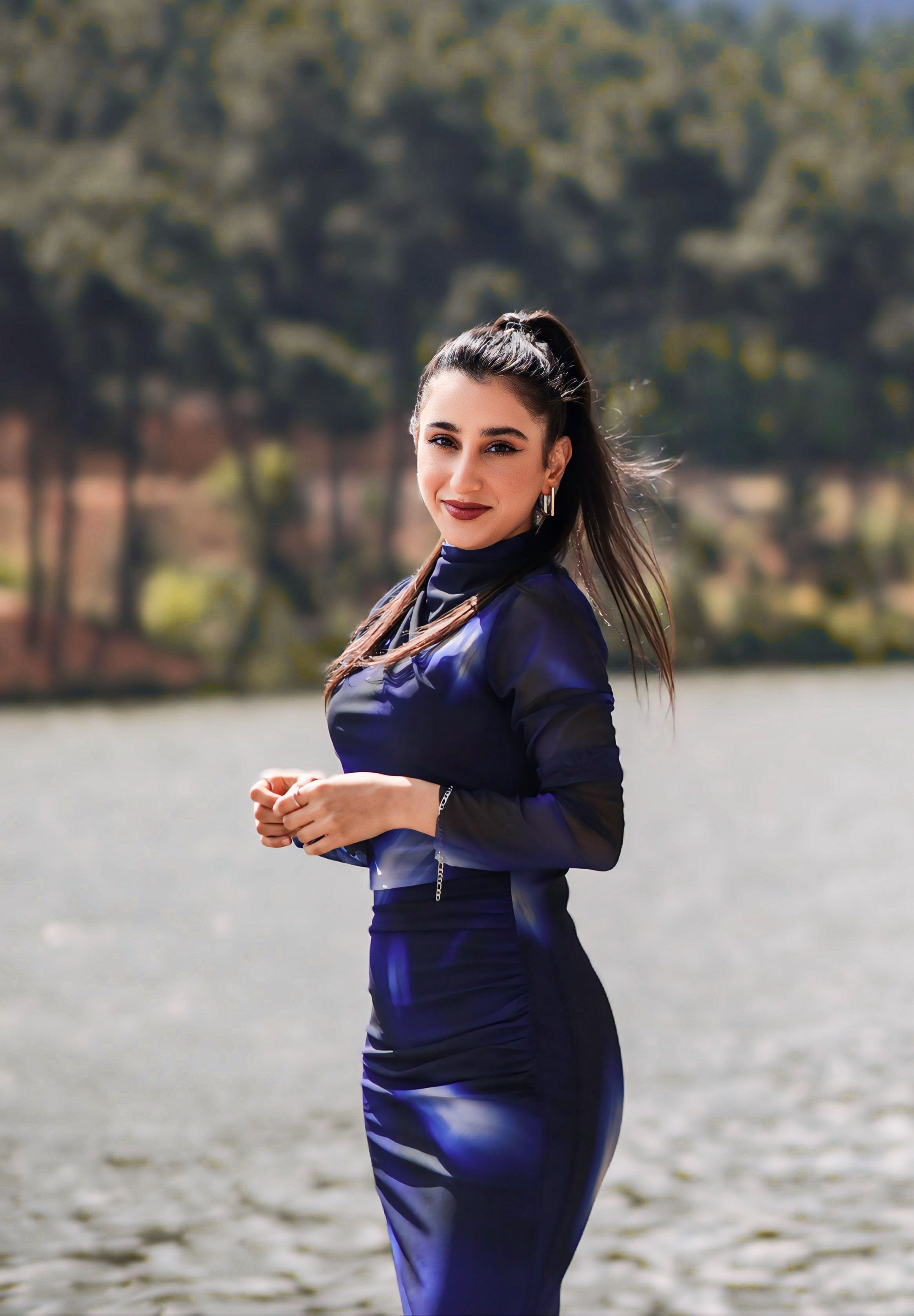 Portrait of a woman in a blue dress standing by a river, showcasing elegance and fashion in natural light.