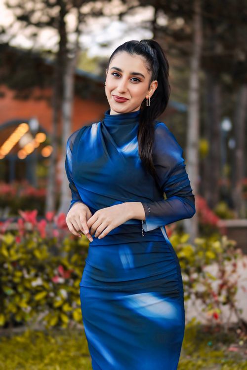 Free A smiling woman in an elegant blue dress posing in a park setting. Stock Photo