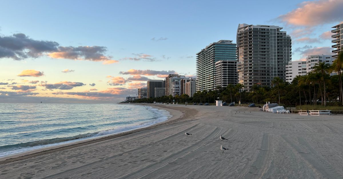 Tranquil evening view of modern architecture along a sandy beach facing the ocean at sunset.