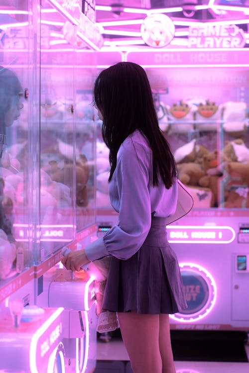 A girl in a skirt looking at a machine with neon lights