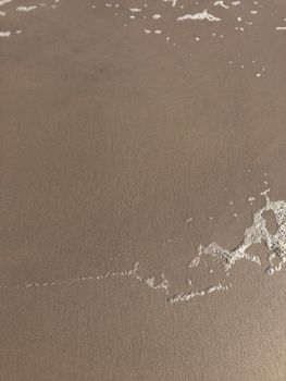 Serene coastal scene featuring smooth sandy beach with gentle foam lapping at the shore.