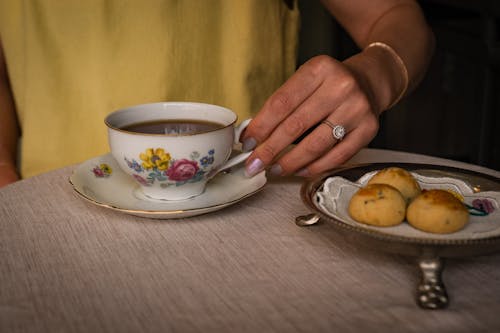 A woman's hand holding a cup of tea and a plate of cookies