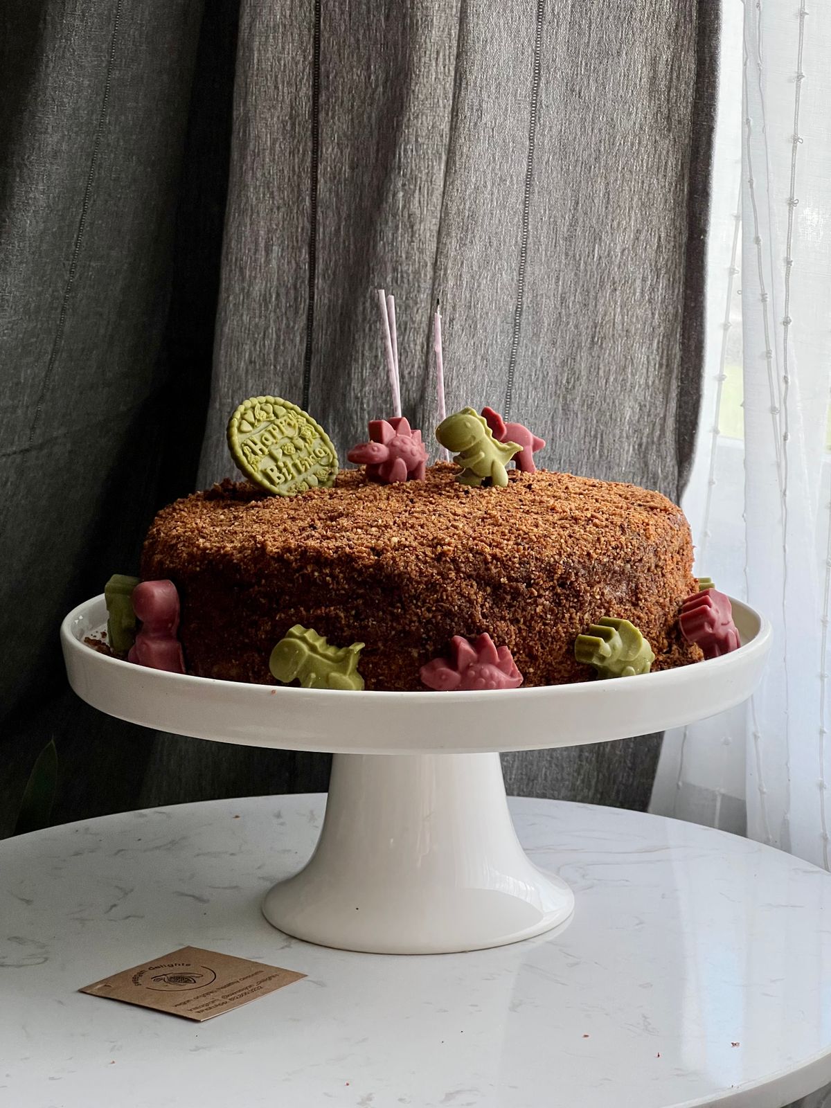 Dinosaur-themed chocolate cake with colorful decorations on a white stand. Stock Photo.