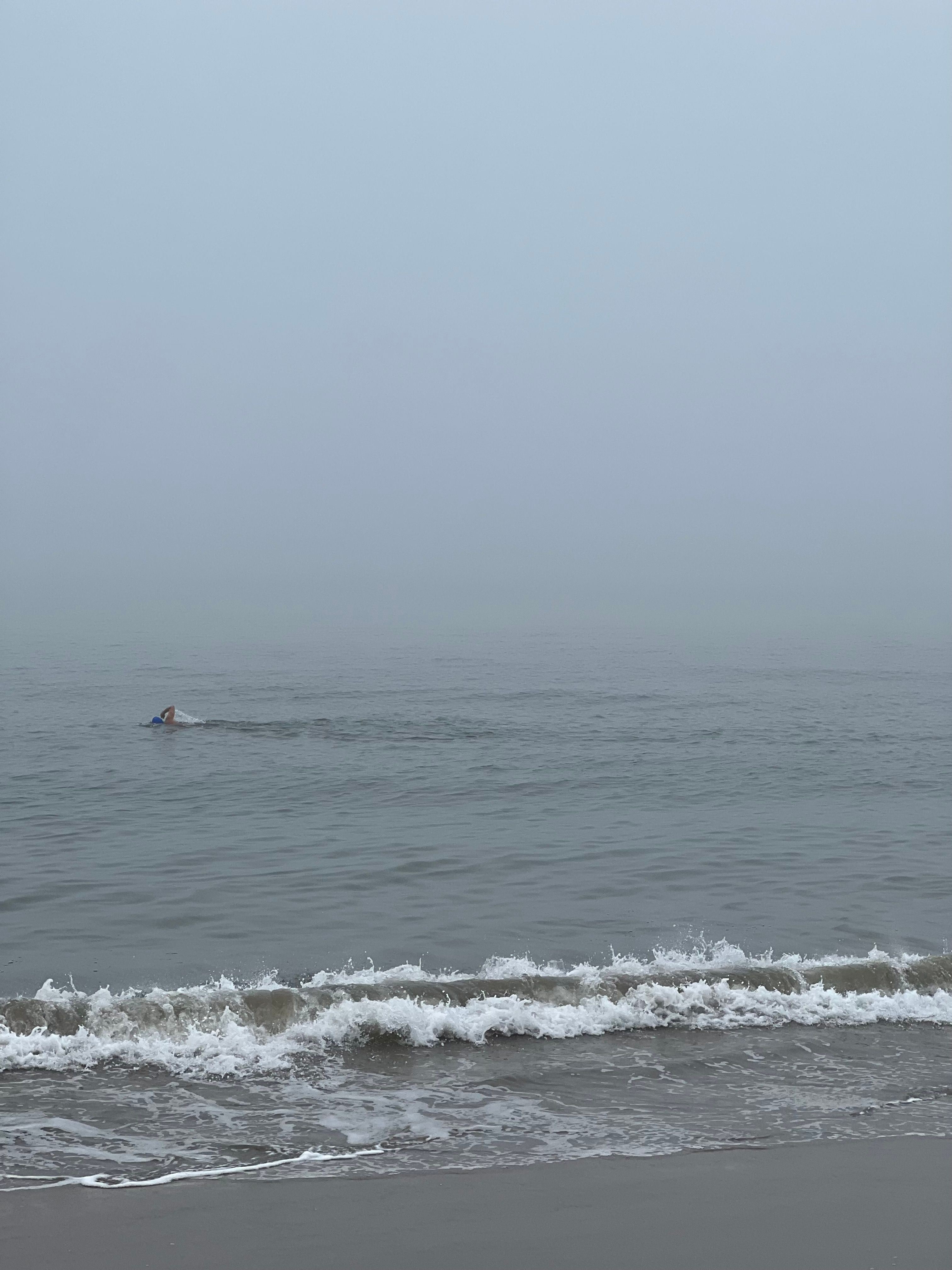 A swimmer in the sea just beyond the breaking waves on a foggy winter morning.