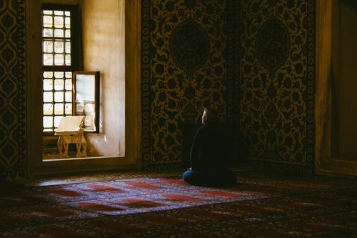 Free A man sits in quiet prayer inside a beautifully decorated mosque, illuminated by soft sunlight. Stock Photo