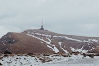 Serene winter landscape of Bucegi Mountains in Romania with a prominent radio mast under cloudy skies.