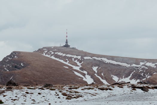 Serene winter landscape of Bucegi Mountains in Romania with a prominent radio mast under cloudy skies.