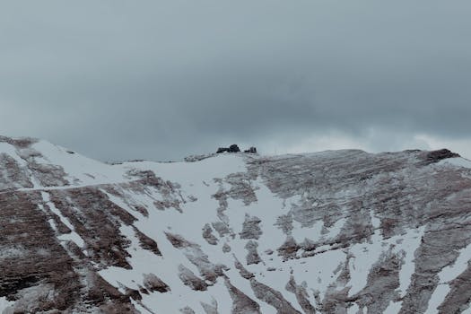 Captivating view of the snow-covered Bucegi Mountains in Bușteni, Romania, under a cloudy sky.