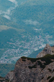Aerial shot of Bușteni village nestled in the Carpathian Mountains surrounded by lush forests.