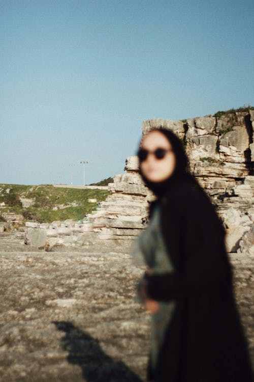 A woman in a black coat and sunglasses standing on a rock