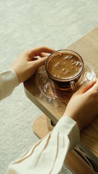 A woman's hands holding a hot coffee cup on a wooden table, creating a cozy indoor vibe.