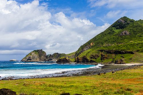 Free Scenic view of a coastal landscape featuring lush green hills, rocky cliffs, and a vibrant blue ocean under a partly cloudy sky. Stock Photo
