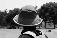 一张灰度照片中，一名戴着帽子、背着背包的成年男子站在户外