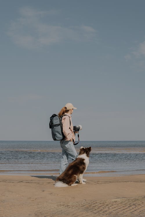 A woman with a backpack and dog on the beach