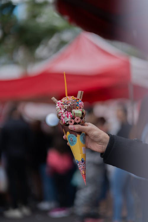 A person holding a small ice cream cone with sprinkles