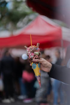 Street vendor's hand holding a delicious bubble waffle with colorful toppings at an urban market.