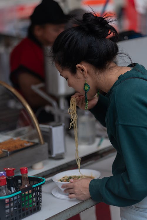 A woman eating noodles at a food stand