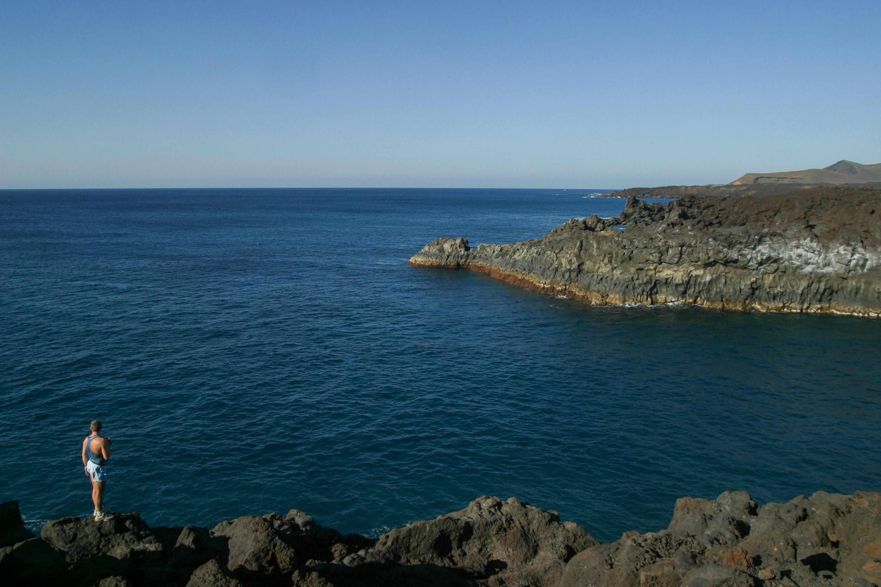 一个人站在悬崖边，欣赏着蔚蓝天空下平静大海的广阔景色