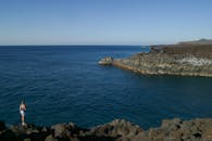 一个人站在悬崖边，欣赏着蔚蓝天空下平静大海的广阔景色