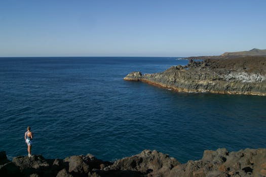 一个人站在悬崖边，欣赏着蔚蓝天空下平静大海的广阔景色