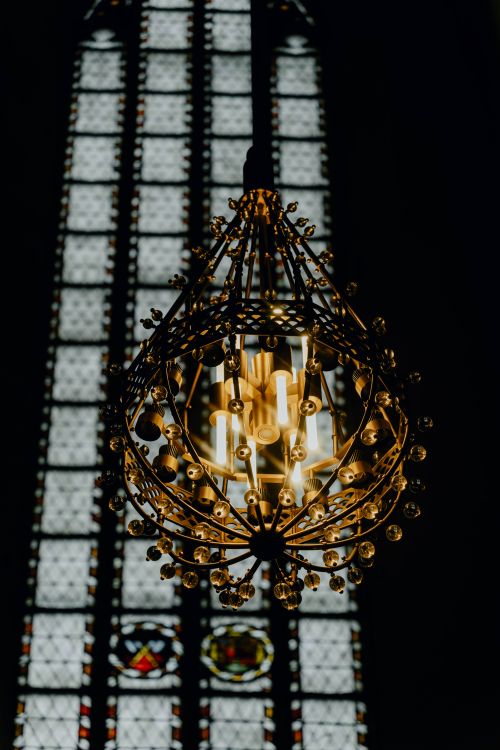 Free Ornate chandelier glowing against the backdrop of stained glass windows in a church in Munich, Germany. Stock Photo