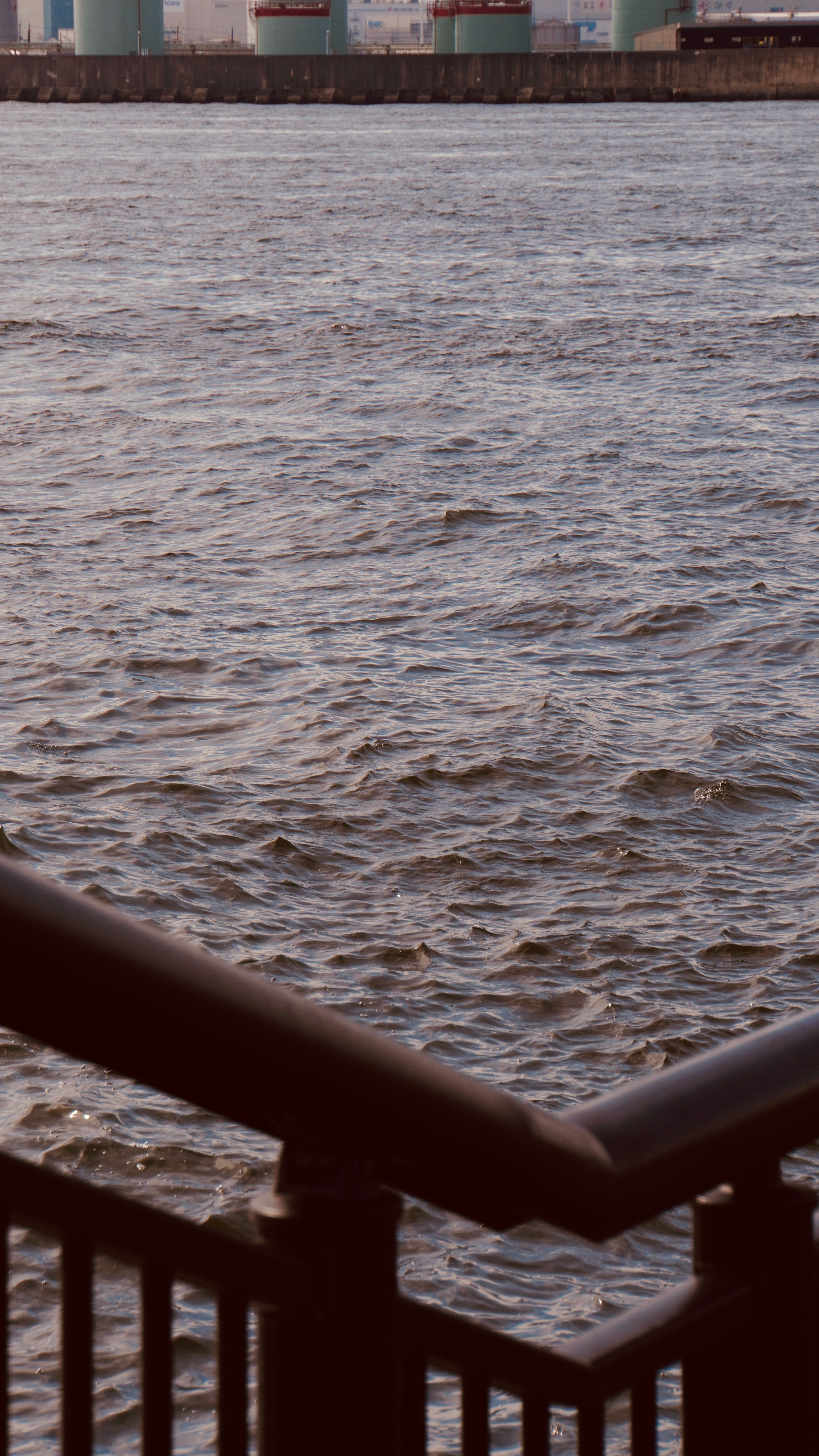 A serene urban waterfront scene with a foreground railing and gentle water ripples.