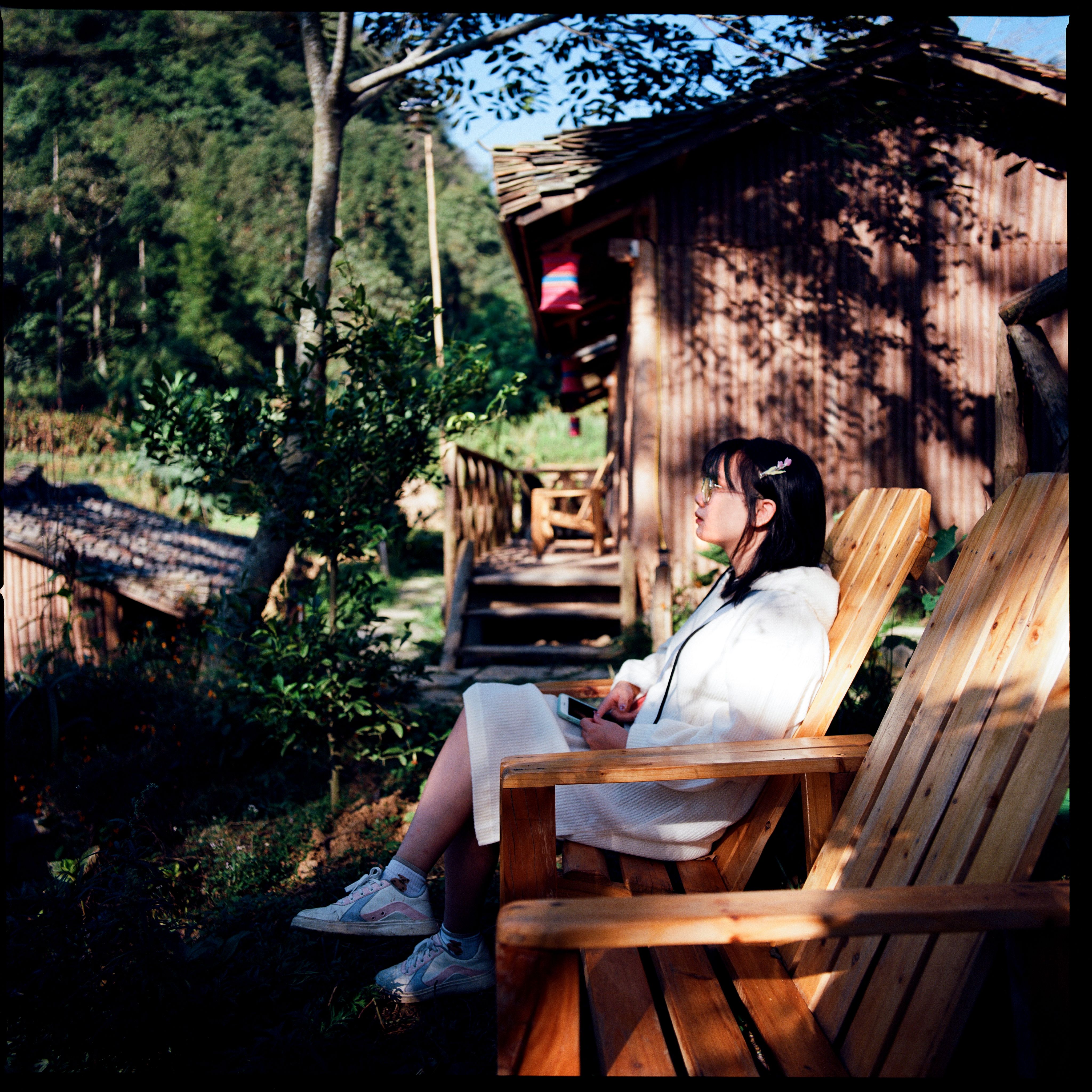 Asian woman embracing tranquility while seated in a wooden chair amidst nature.