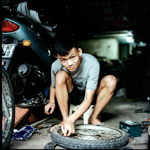 A young man is kneeling down in front of a motorcycle