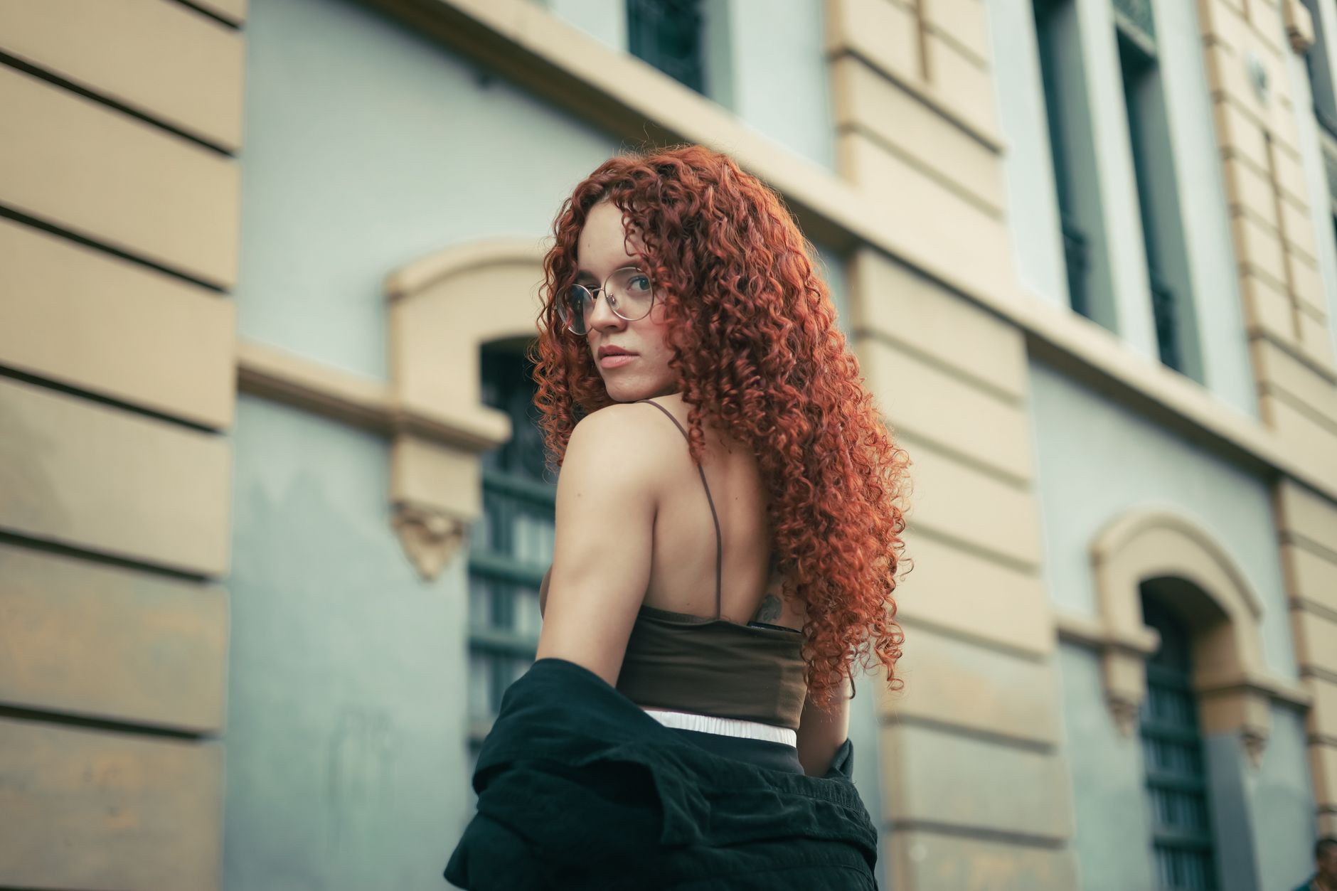 Portrait of a young woman with red curls posing on a city street, glancing to the side