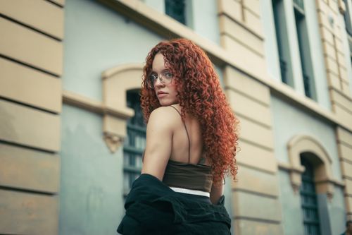 Free Stylish portrait of a young woman with red curls, posing outdoors in a city context. Stock Photo