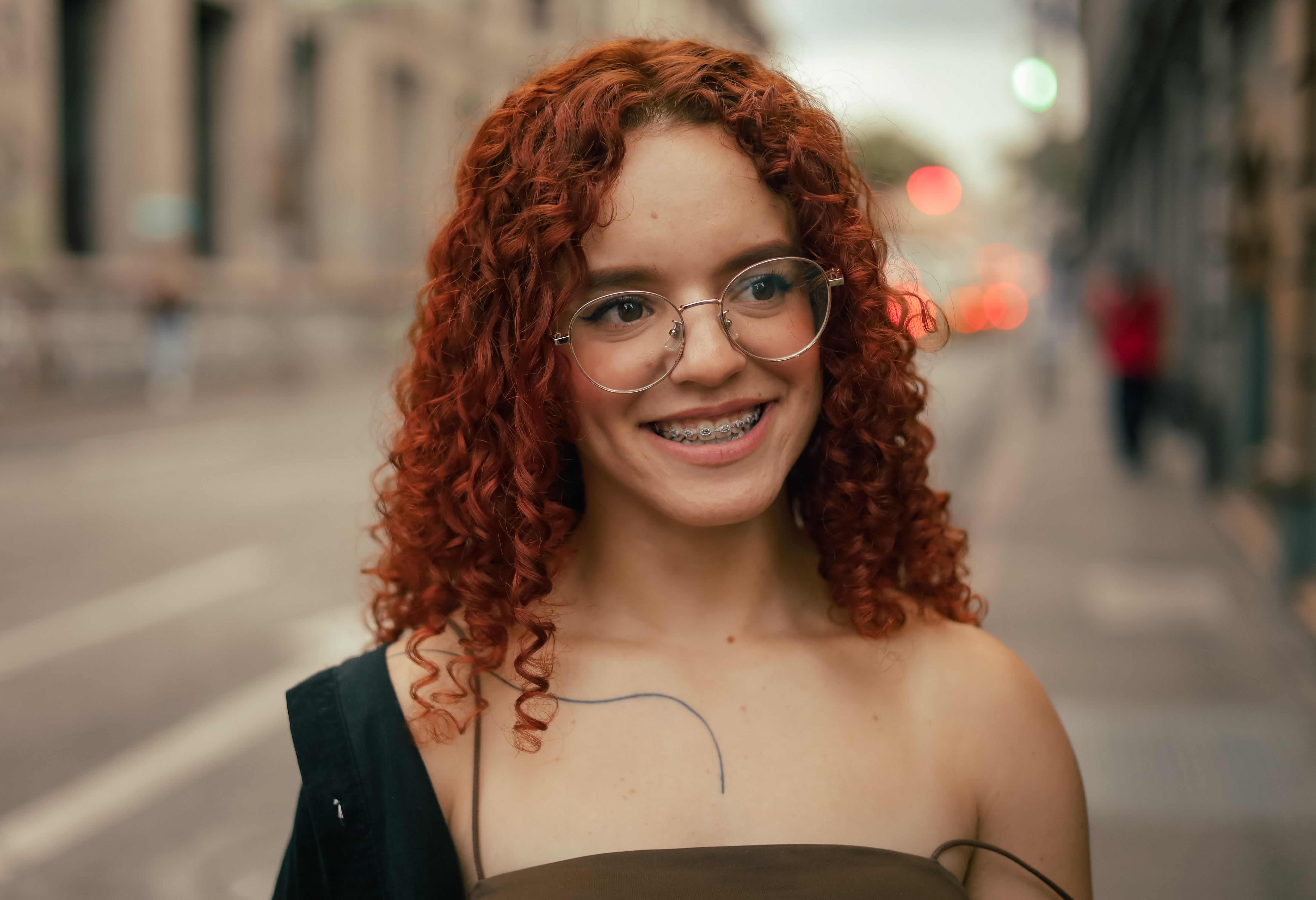 A woman with curly red hair smiling in the street · Free Stock Photo