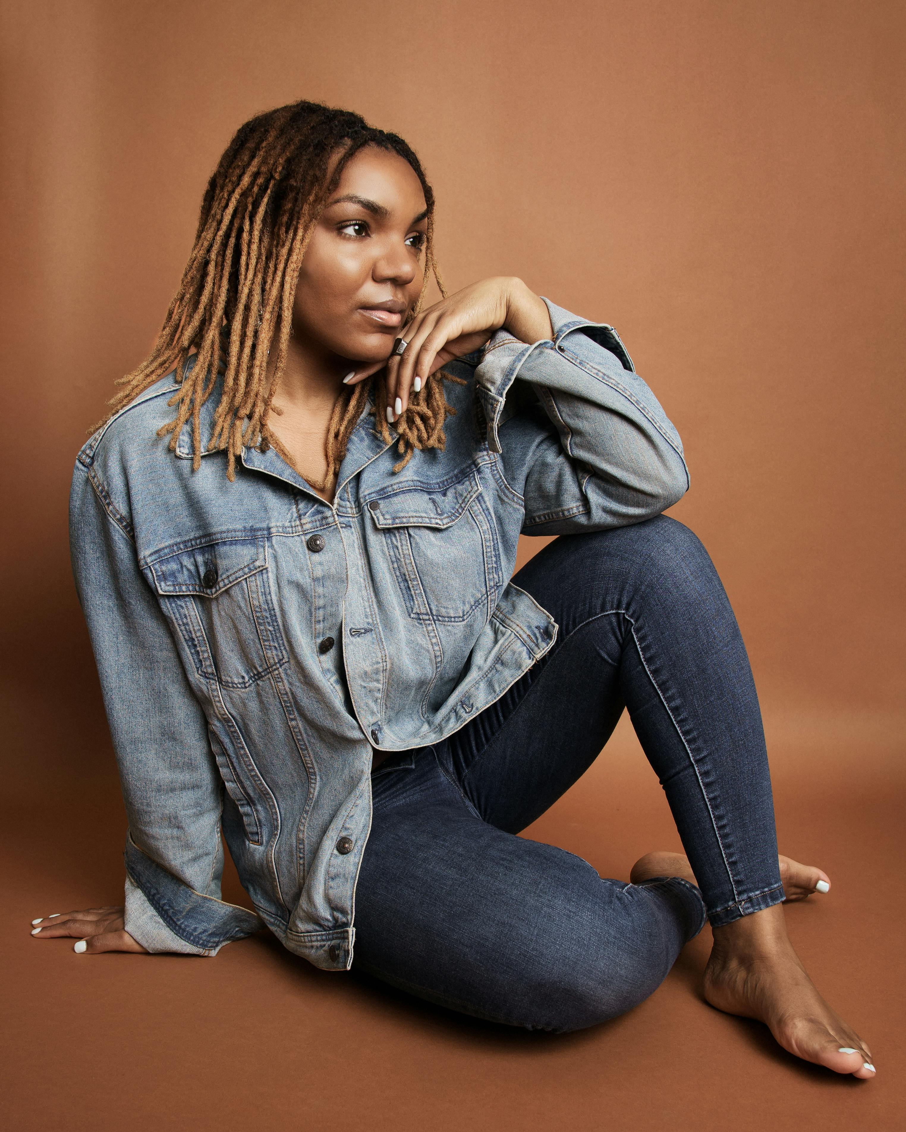 Young woman with dreadlocks posing in a denim jacket in a studio.