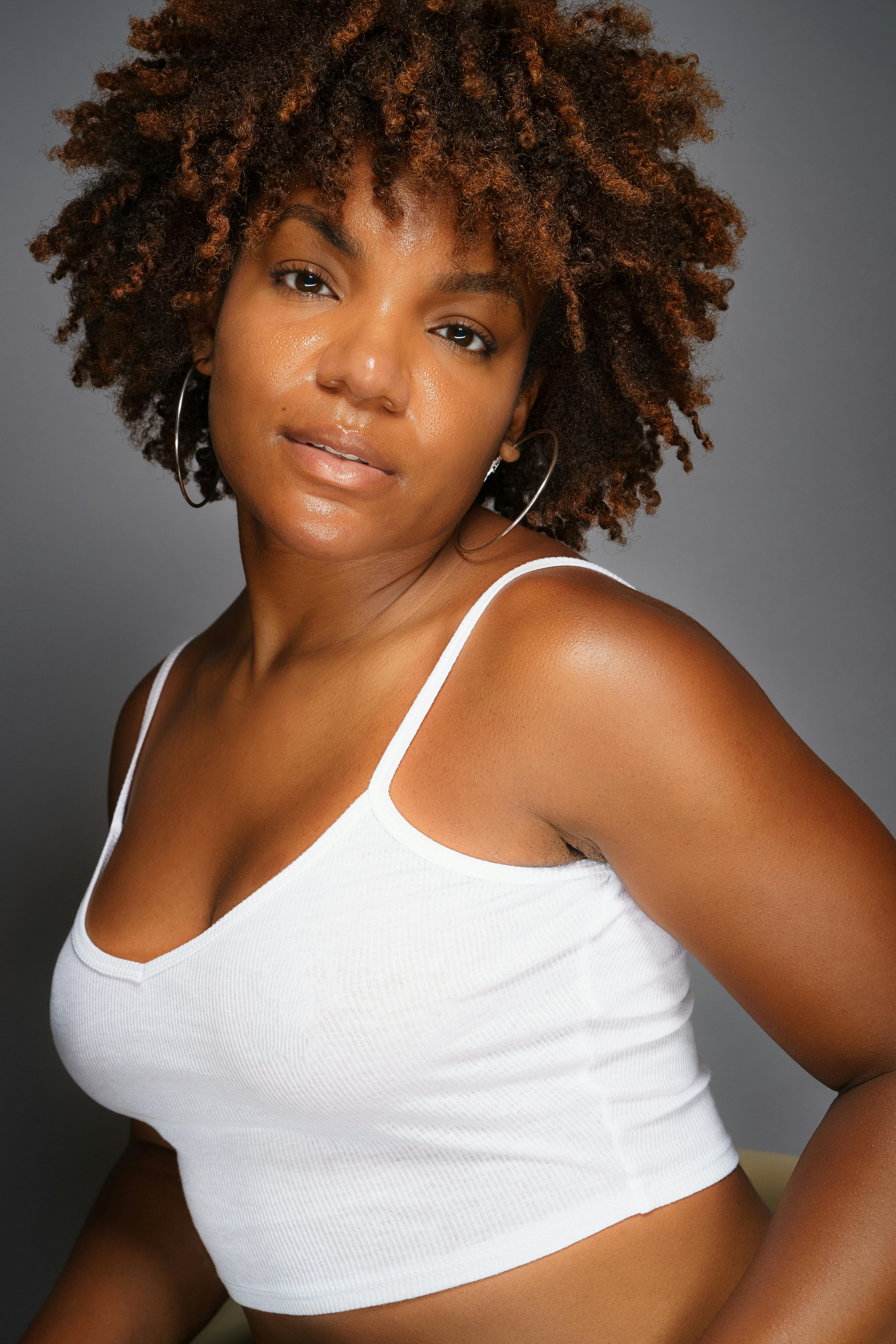 Close-up portrait of a woman with afro hairstyle in a white top, exuding confidence.