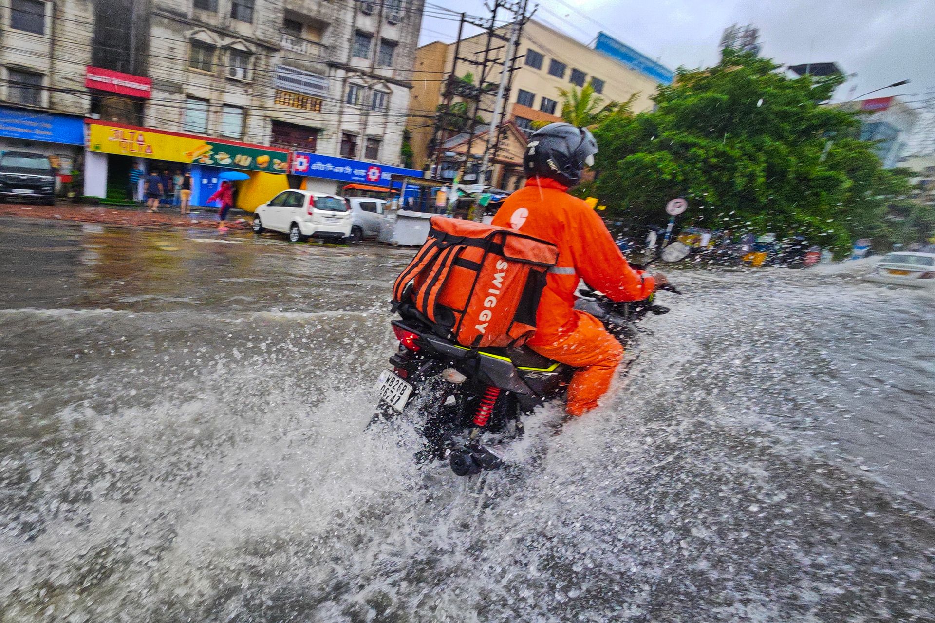 A delivery person on a motorcycle navigates flooded streets of Kolkata, India, during rain.