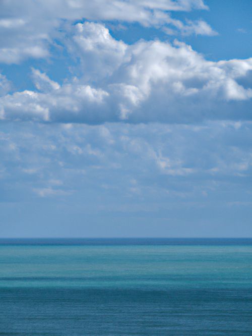 Free A peaceful ocean scene with fluffy white clouds against a blue sky, creating a tranquil seascape. Stock Photo