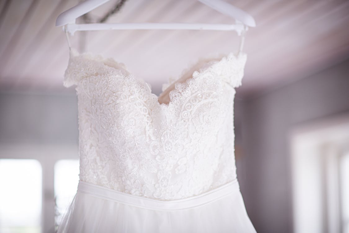 A wedding dress with lace detailing hangs in a room