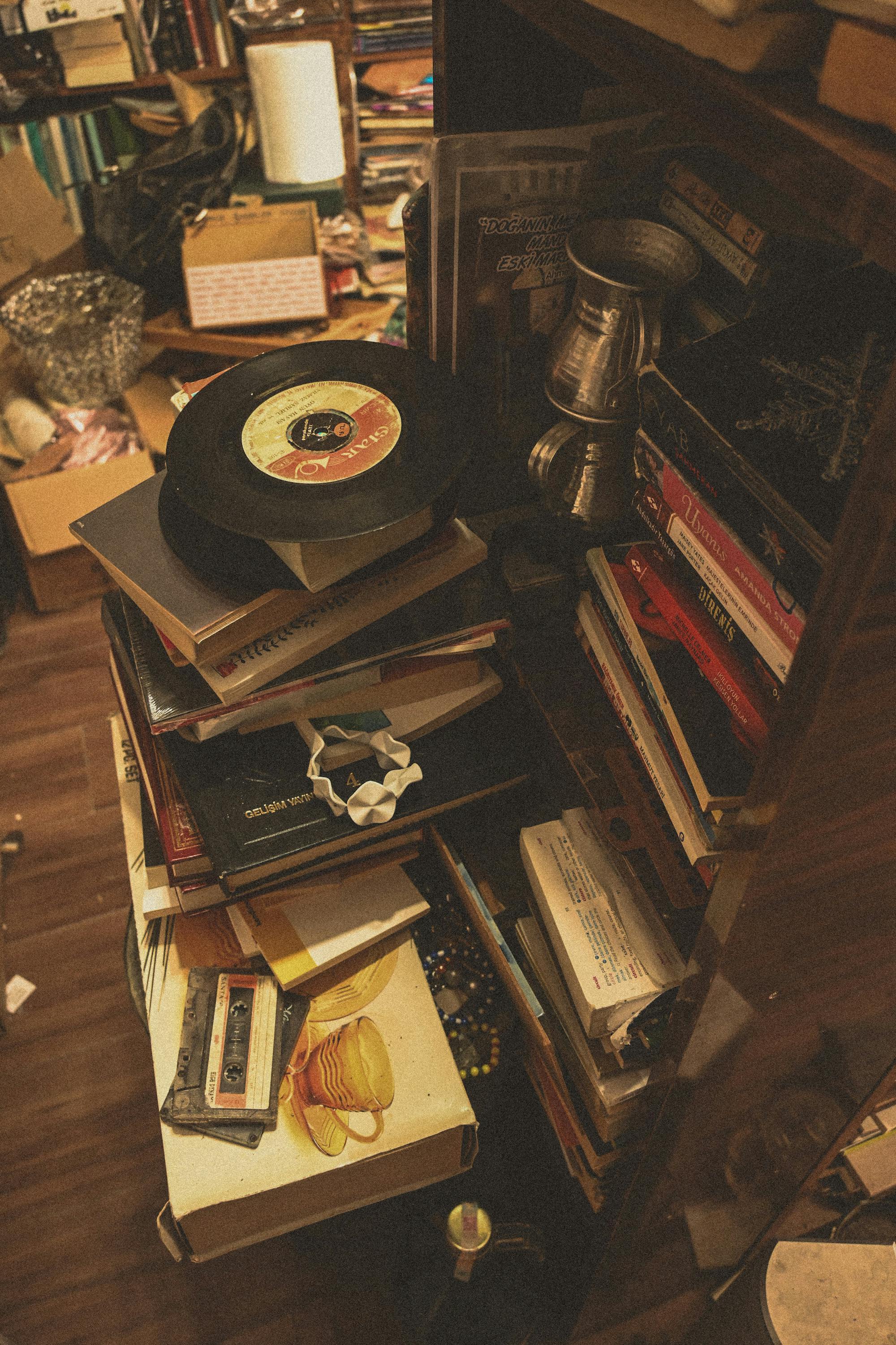 A cozy cluttered corner with vintage vinyl records, books, and cassettes in a retro shop setting.