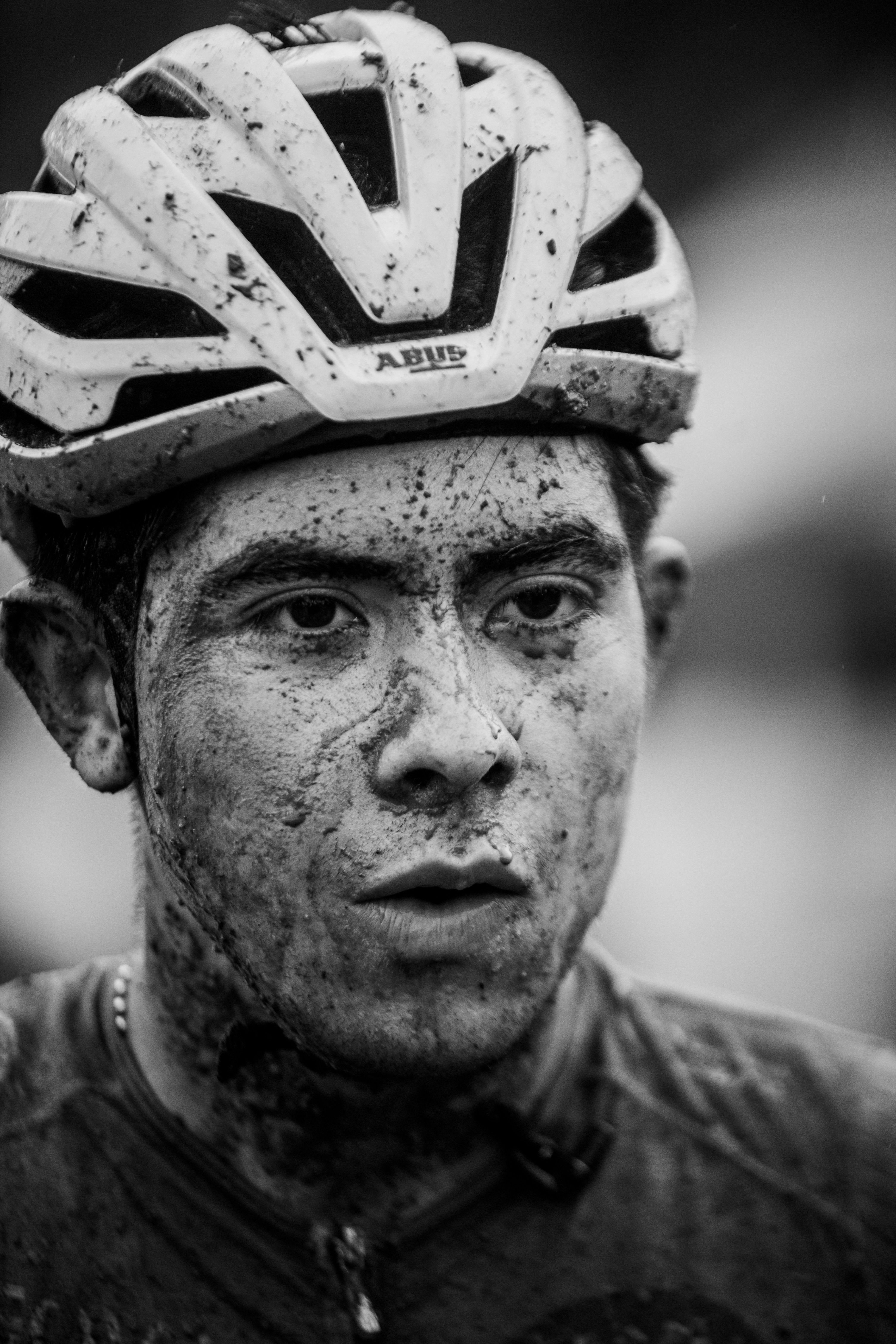 Black and white portrait of a muddy cyclist wearing a helmet, showcasing determination.