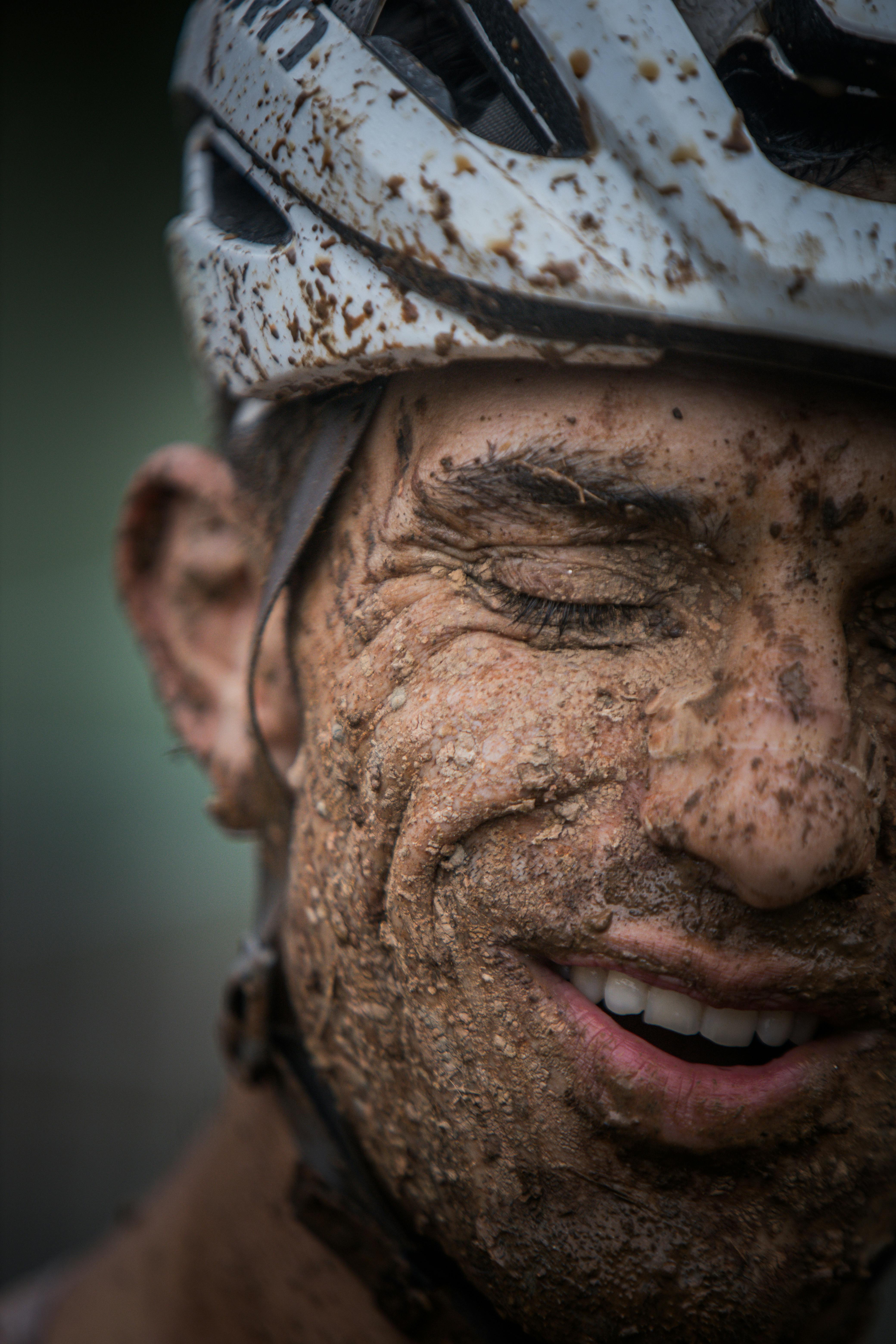 Muddy cyclist in helmet smiling after an intense outdoor biking session.